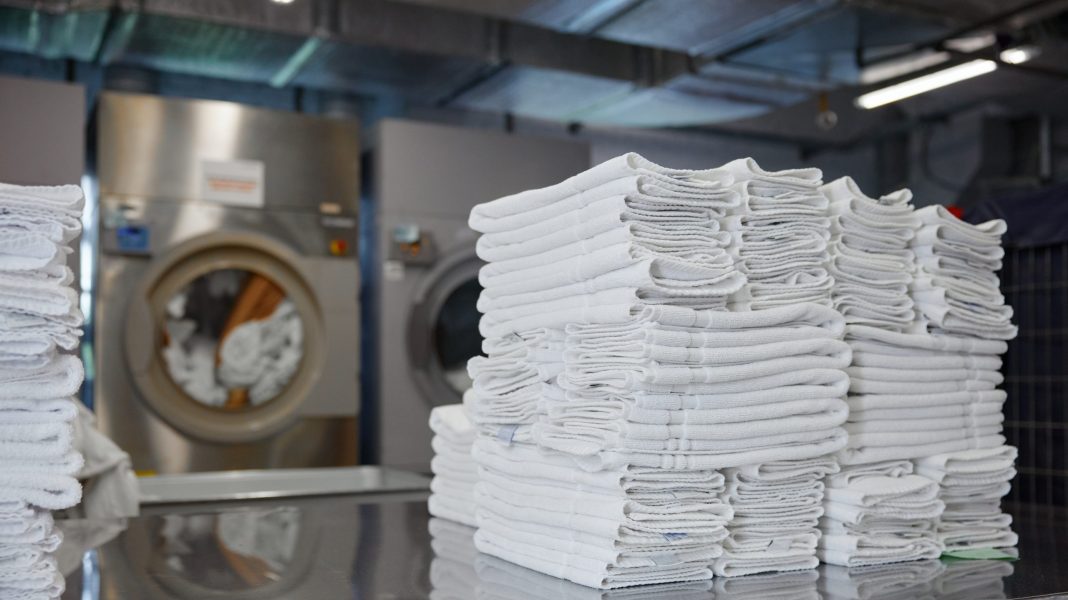 In the laundry room, a neat stack of clean white towels is placed on the table directly in front of a washing machine, ready for use